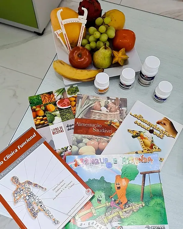 Frutas, frascos de suplemento e materiais de orientação alimentar sobre a mesa do consultório