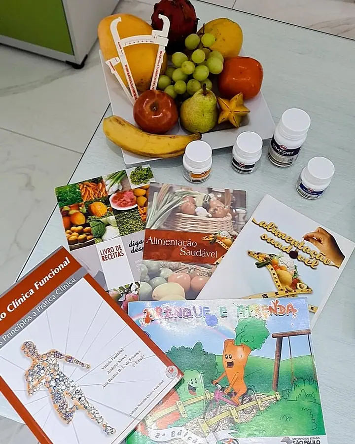 Frutas, frascos de suplemento e materiais de orientação alimentar sobre a mesa do consultório