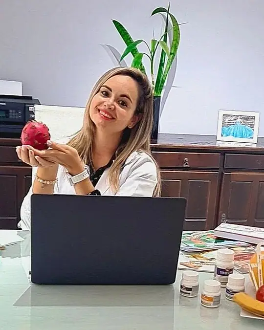 Natacha Ludkiewicz, nutricionista funcional, segurando uma maçã à mesa do consultório