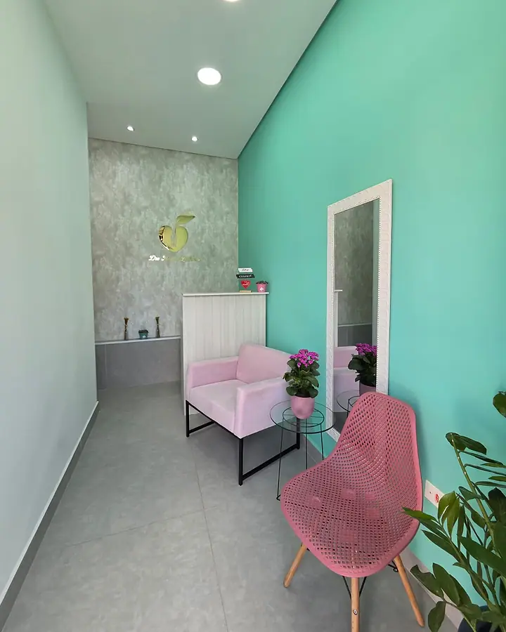 Recepção do consultório, com poltronas rosa, espelho e parede verde-água