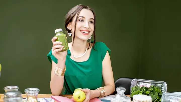Mulher à mesa com garrafa de suco verde, frutas e verduras