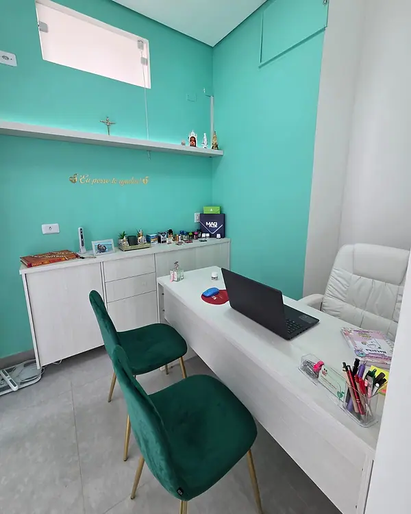 Sala de atendimento com mesa branca, cadeiras verdes e parede verde-água