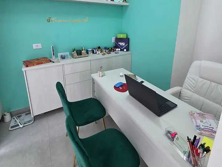 Mesa de consulta com notebook e duas cadeiras verdes no consultório