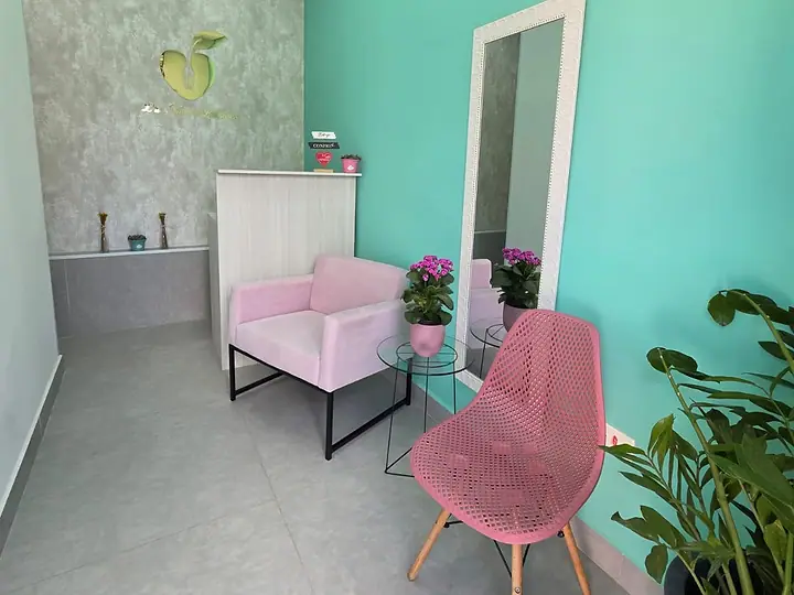 Sala de espera do consultório, com parede verde-água, poltronas rosa e flores