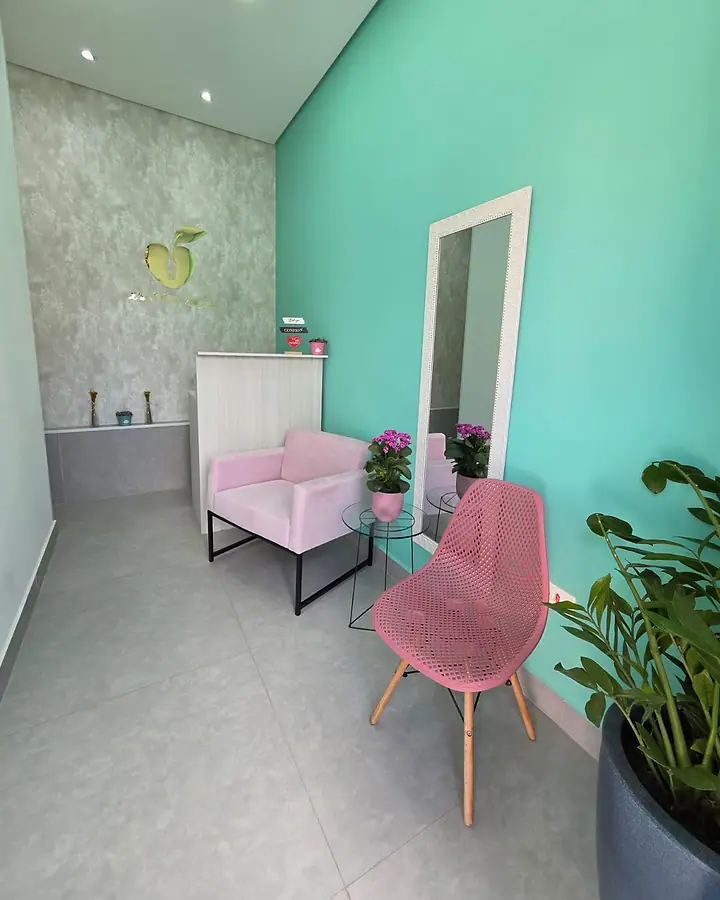 Sala de espera do consultório, com parede verde-água, poltronas rosa e flores